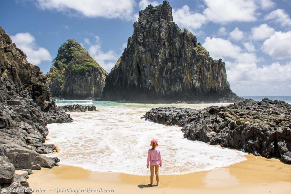 Imagem de uma menina admirando as espumas brancas das ondas da praia.